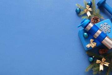 Composition with bottle of water, sports equipment and Christmas decorations on blue background