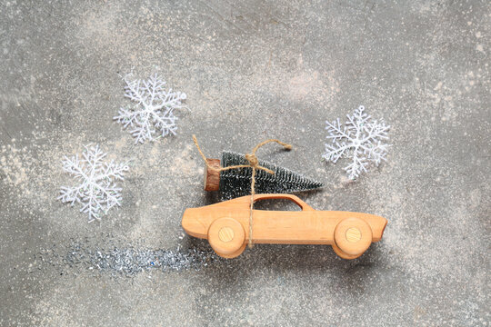 Toy wooden car with small Christmas tree and snowflakes on grey background