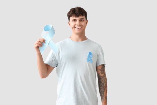 Young man with blue ribbon on light background. Prostate cancer awareness concept