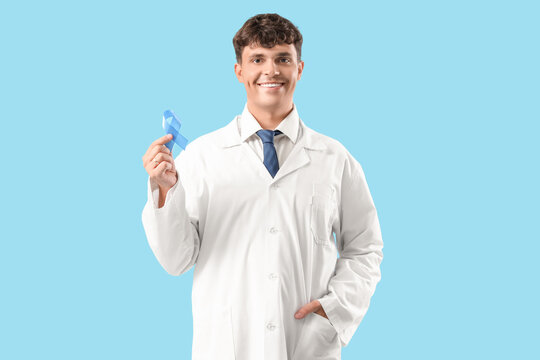 Male doctor with blue ribbon on color background. Prostate cancer awareness concept