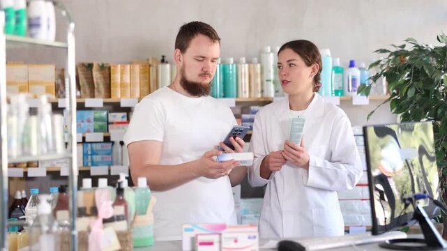Young man buyer scanning qr code for box of ointment with young woman pharmacist in pharmacy