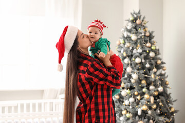 Mother kissing her little baby dressed as elf in bedroom on Christmas eve