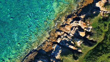 Aerial view of rugged coastline with turquoise waters, rocky cliffs, and lush greenery. Pristine beach highlights untouched beauty, inviting exploration and adventure.