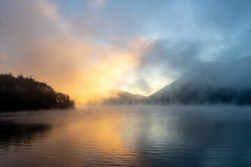 A mystical mist quietly covers the lake surface at dawn