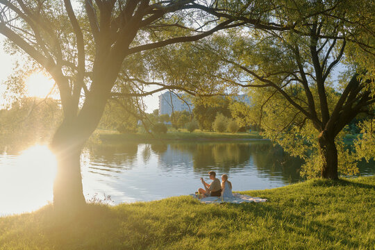 Couple enjoying a picnic beside a tranquil pond during a sunny afternoon in a park