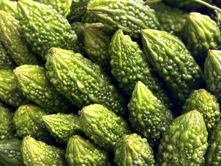 High-angle close-up of fresh green bitter gourds (karela) piled together. Their elongated, warty, bumpy texture fills the frame, showcasing the distinct look of this tropical edible fruit.