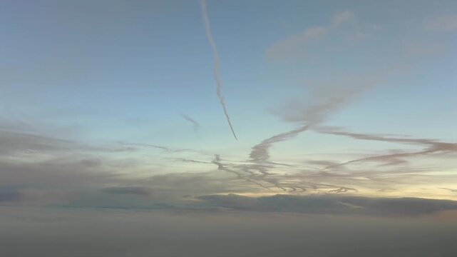 Immersive cockpit view flying at dawn in a serene pastel color sky, with some clouds in the horizon, and some jet contrails fading above in the upper atmosphere.