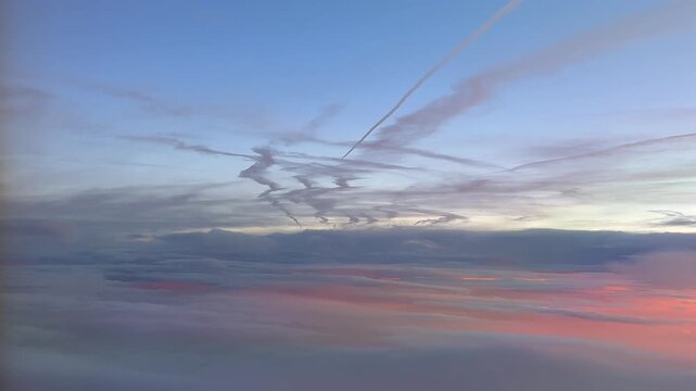 An aerial view taken from a jet cockpit at dawn flying under multiple contrails fading in a pastel color sky, and golden clouds bellow.