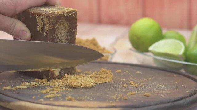 Preparing a traditional recipe, shaving jaggery with a knife on a wood board