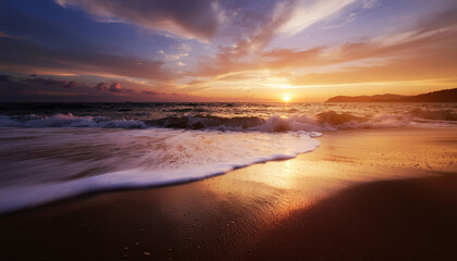Obraz premium Golden hour sunset paints the sky with vibrant hues over a tranquil ocean, waves gently lapping the sandy shore creating a serene, breathtaking seascape.