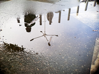 Reflective puddle mirrors abstract shapes and human figure in muted tones and rainy ambiance.