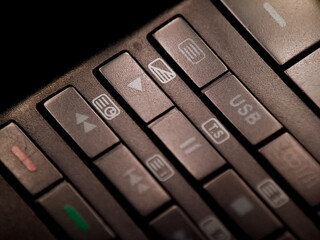 A dimly illuminated remote control displays buttons with symbols for media playback features.