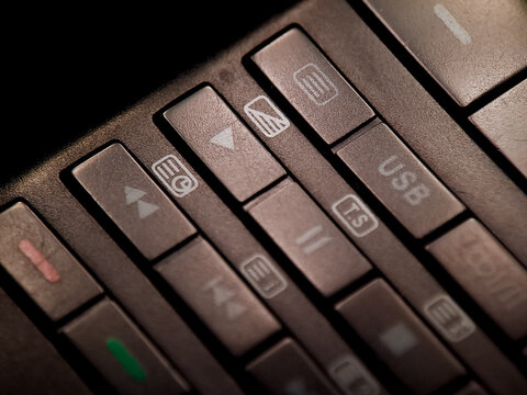 A dimly illuminated remote control displays buttons with symbols for media playback features.