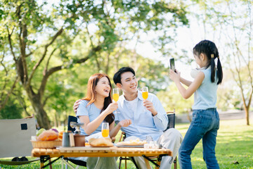 Joyful family enjoying coffee and snacks during a picnic in a sunny green park. A warm, happy lifestyle moment full of love, laughter
