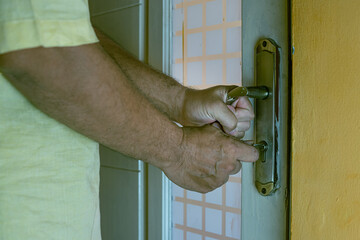 Close-up of a hand inserting a key into an old rusty door lock, symbolizing security, access, and safety concepts, landscape