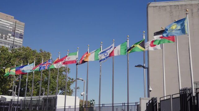 Row of national flags waving outside the United Nations Headquarters in New York City, New York under clear blue sky representing global unity, diplomacy and international cooperation. USA
