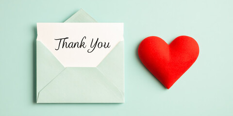 Still life of thank you card in envelope with red heart on a light green background surface