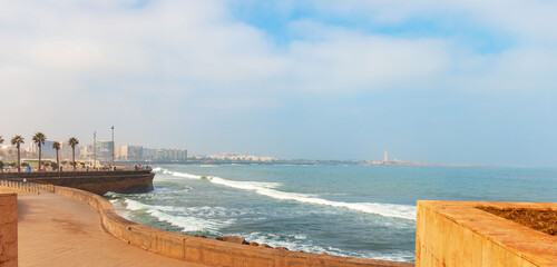 Atlantic Ocean promenade with waves, palm trees, and city skyline view in Casablanca, Morocco. © Анастасия Бабак