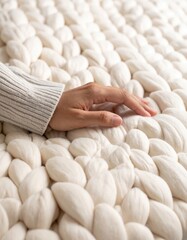 Hand touching soft chunky knitted blanket in neutral bedroom setting.