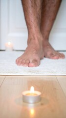 Bare feet standing near small candle on wooden floor in cozy home setting.