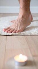 Bare feet near burning candle on light rug in soft daylight.