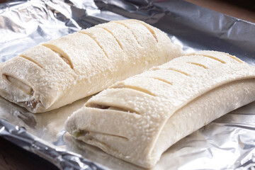 Raw apple strudels, with sliced pastry, on foil ready for cooking in an oven. Home baking concept