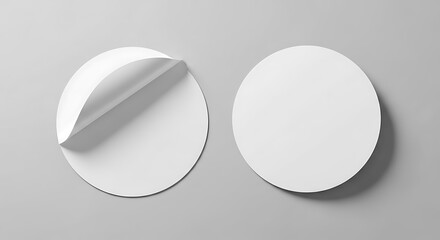 Two white, round stickers. One is partially peeled, revealing adhesive. The other is whole. Placed on a grey backdrop