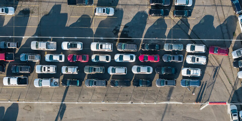 Obraz premium Aerial view of many cars with long shadows for sale at large outdoor dealership parking lot in USA.