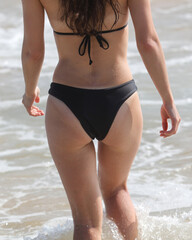 A woman is walking on the beach wearing a black bikini