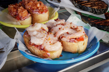 Shrimp bruschetta at street food market. Raw seafood appetizer, concept of mediterranean diet, italian food, or tapas. Close up of fresh prawns on toast.