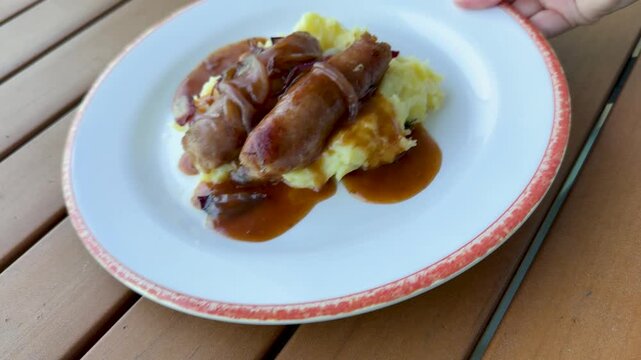 Serving a Plate of Bangers and Mash ( British Sausages and Mashed Potatoes with onion Gravy)