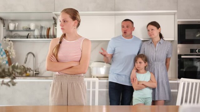 At home kitchen, parents scold daughter for careless act. Sulky preschool girl sit near table during serious conversation with parents