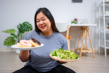 Asian young plus-size woman deciding between green salad and donut. 