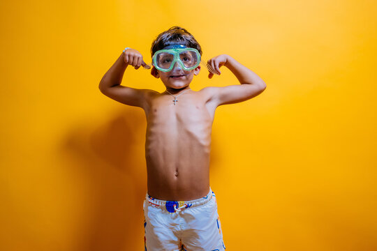 Child wearing swim goggles posing with flexed arms.
