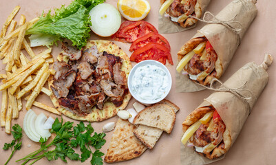 Greek gyros wraps and fresh ingredients arranged upon the rustic table under natural daylight, showing pita bread, grilled meat, fries, vegetables, and tzatziki sauce within a warm inviting setting