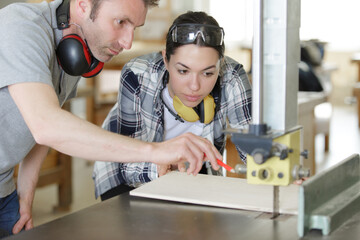 carpenter training female apprentice to use mechanized saw