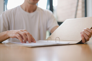 Close up of a man reading documents in a binder at a desk, representing office work, document review, or business analysis in a modern workspace.