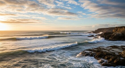 Coastal scene during golden hour, with waves crashing on rocks, under a partly cloudy sky