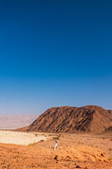 A female tourist with a backpack walks through the desert, enjoying the view of the red rocks and canyon gorges. Desert trip. Timna National Park. Israel.