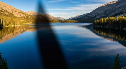 A serene lake reflects the surrounding mountains and trees under a clear, sunny sky