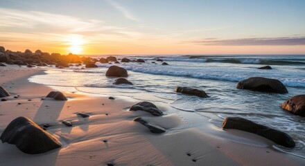 Sunrise over sandy beach with boulders, gentle waves, and a colorful, calm sky