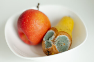 Moldy pear with mold and fresh apple on plate