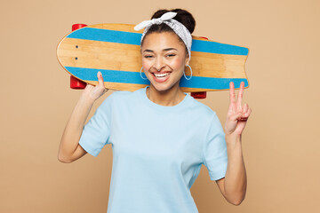 Young smiling fun woman of African American ethnicity wear blue t-shirt casual clothes hold skateboard pennyboard behind head isolated on plain pastel light beige background studio. Lifestyle concept.