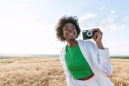 Happy afro woman holding camera in field