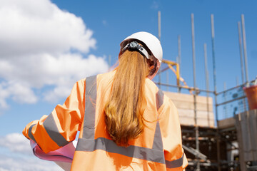 Builder woman working on construction site and using drawings to check works progress