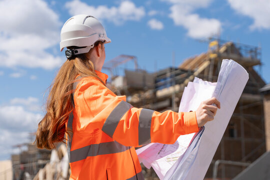 Builder woman working on construction site and using drawings to check works progress