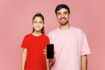 Young parent man with child girl wear red casual clothes. Daddy little kid daughter hold mobile cell phone with blank screen area isolated on plain pink background. Father's Day Love family concept.