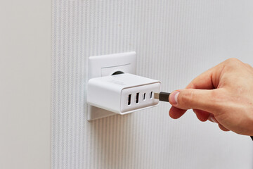 male hand insert a plug of the phone charger into socket at home