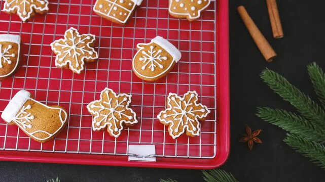 Decorated holiday cookies cooling on a red baking sheet with spices and pine branches