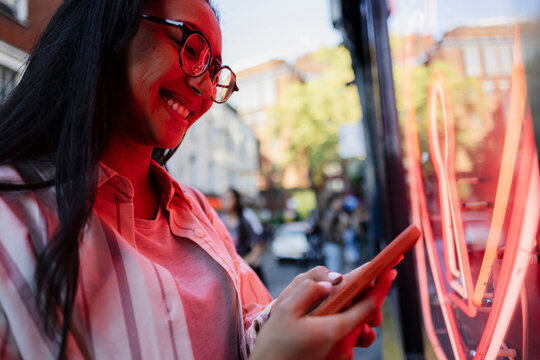 Smiling woman with glasses using smartphone in city street at day